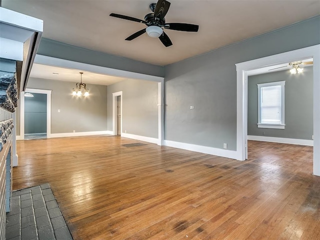 unfurnished living room with ceiling fan, a chandelier, hardwood / wood-style flooring, and baseboards