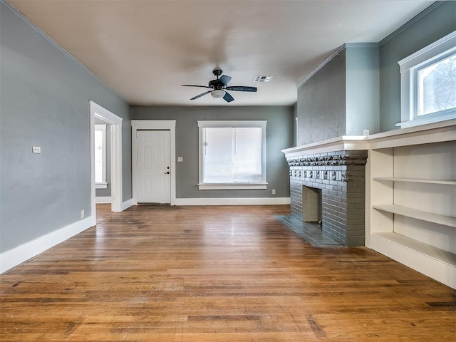 unfurnished living room featuring a brick fireplace, a ceiling fan, wood finished floors, baseboards, and ornamental molding