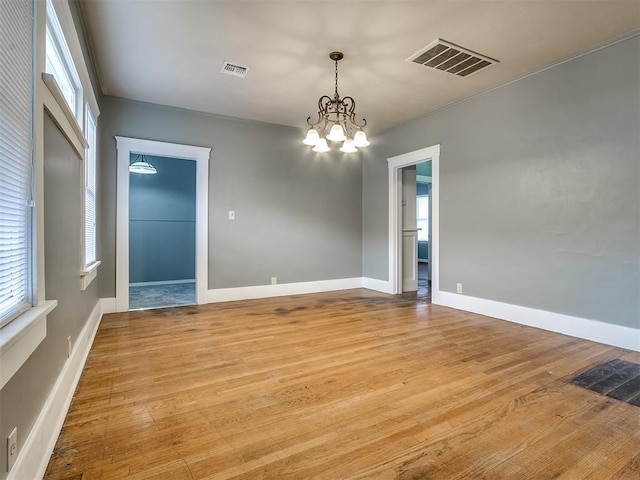 spare room with a chandelier, plenty of natural light, light wood-type flooring, and baseboards