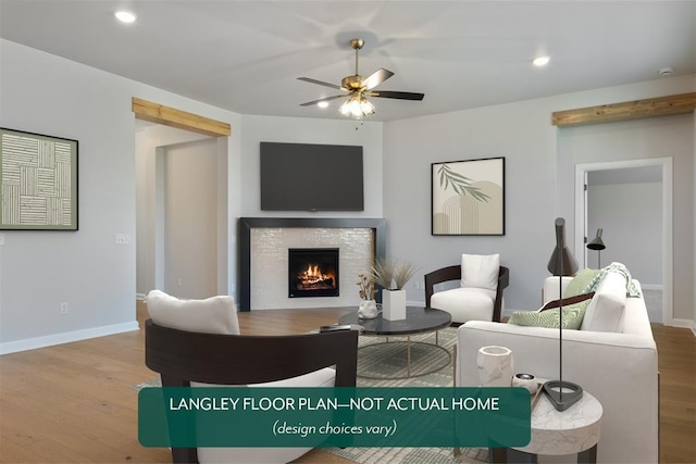 living room featuring wood finished floors, baseboards, a warm lit fireplace, recessed lighting, and a ceiling fan