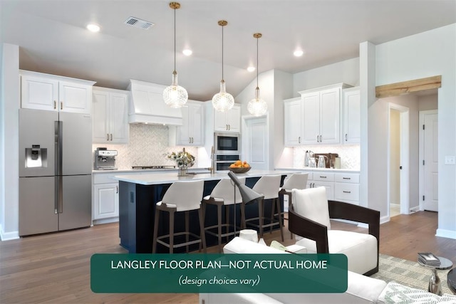 kitchen with stainless steel appliances, premium range hood, tasteful backsplash, a breakfast bar area, and a kitchen island with sink