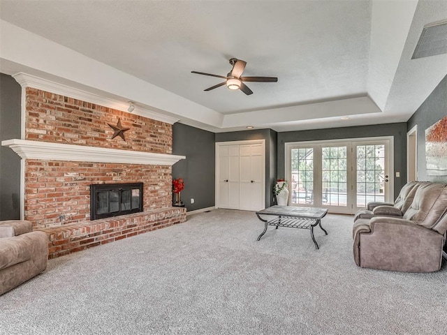 1409 Echohollow Trl, Edmond, OK 73025 - carpeted living area with a ceiling fan, a tray ceiling, a brick fireplace, and baseboards