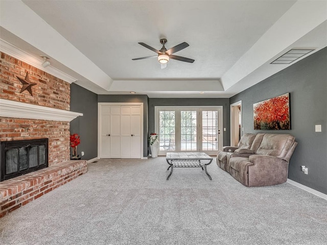 1409 Echohollow Trl, Edmond, OK 73025 - carpeted living area featuring a raised ceiling, a ceiling fan, baseboards, and a brick fireplace