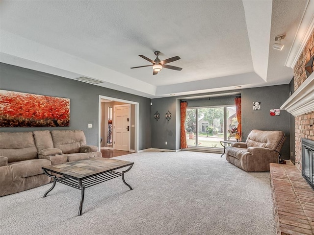 1409 Echohollow Trl, Edmond, OK 73025 - carpeted living area featuring a fireplace, a textured ceiling, a ceiling fan, a tray ceiling, and baseboards