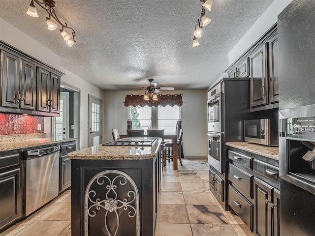 1409 Echohollow Trl, Edmond, OK 73025 - kitchen featuring stainless steel appliances, a kitchen island, track lighting, ceiling fan, and decorative backsplash