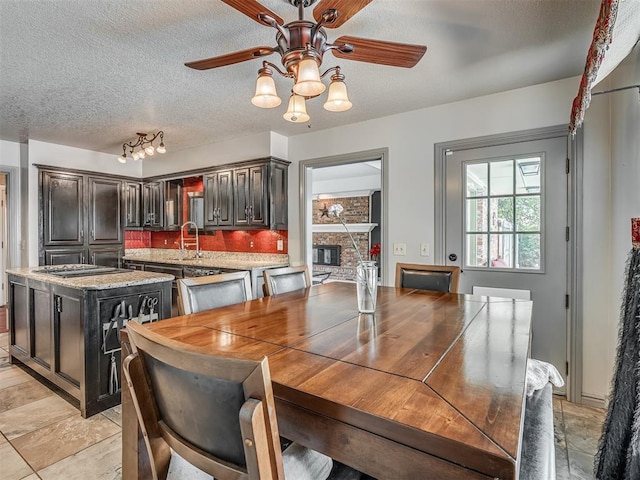 1409 Echohollow Trl, Edmond, OK 73025 - dining room featuring ceiling fan, a textured ceiling, a large fireplace, and light stone finish floors