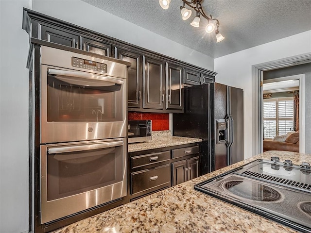 1409 Echohollow Trl, Edmond, OK 73025 - kitchen with black appliances, light stone counters, a textured ceiling, dark brown cabinets, and decorative backsplash