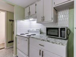 2624 N Ann Arbor St Unit 106, Oklahoma City, OK 73127 - kitchen featuring white electric stove, stainless steel microwave, under cabinet range hood, light stone counters, and tasteful backsplash