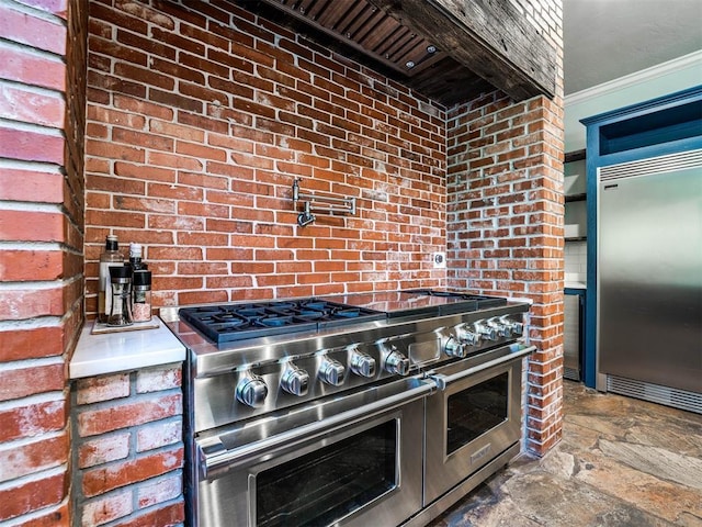 kitchen with high end appliances, stone finish floors, ornamental molding, and brick wall