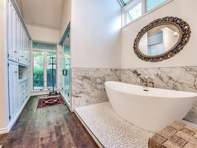full bath featuring tile walls, a wainscoted wall, a stall shower, wood finished floors, and a soaking tub