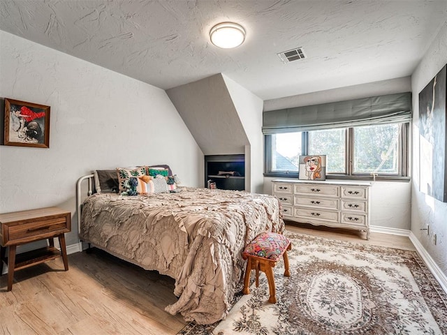 bedroom featuring light wood-style flooring, baseboards, a textured ceiling, and vaulted ceiling