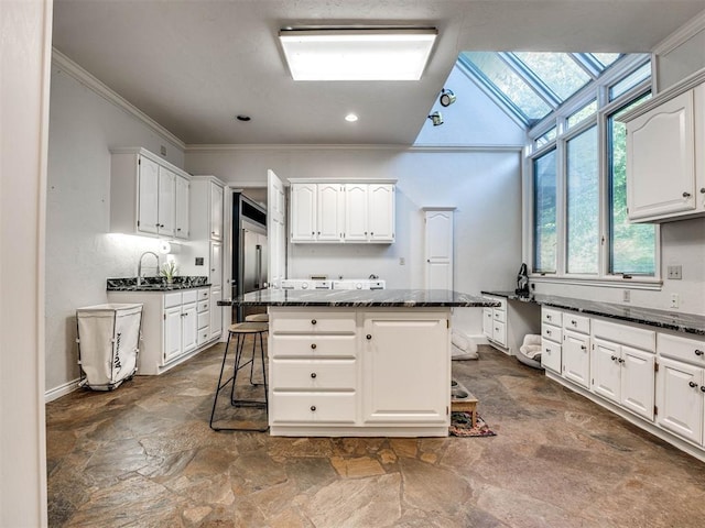 kitchen featuring dark stone finish floors, crown molding, a breakfast bar, a skylight, and white cabinetry