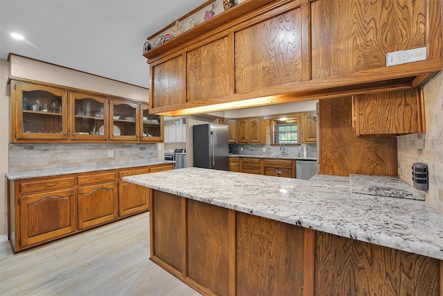 11747 N 2240th Rd, Cordell, OK 73632 - kitchen with appliances with stainless steel finishes, brown cabinets, tasteful backsplash, a peninsula, and light wood finished floors