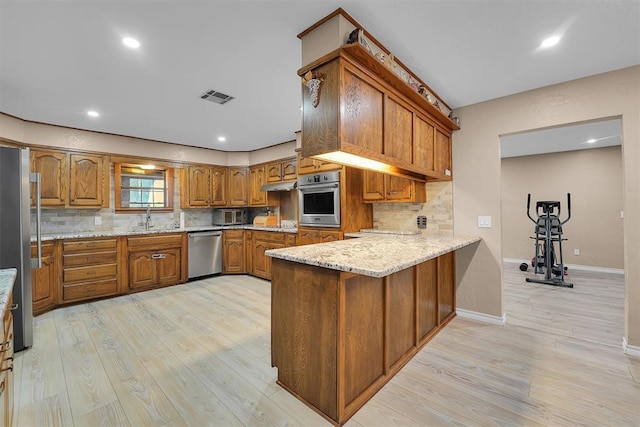 11747 N 2240th Rd, Cordell, OK 73632 - kitchen with stainless steel appliances, brown cabinets, a peninsula, light wood finished floors, and decorative backsplash