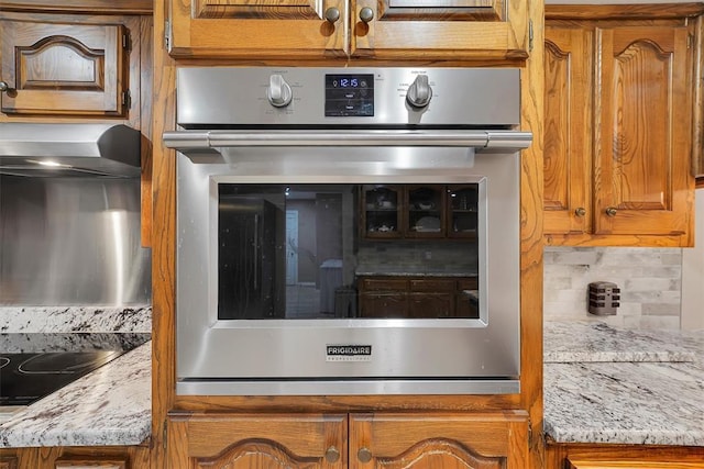 11747 N 2240th Rd, Cordell, OK 73632 - kitchen view of stainless steel oven, decorative backsplash, brown cabinetry, and light stone counters