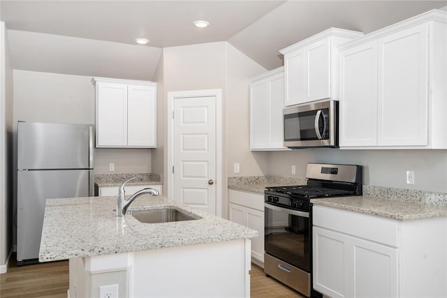 kitchen with stainless steel appliances, a sink, light wood-type flooring, white cabinetry, and vaulted ceiling