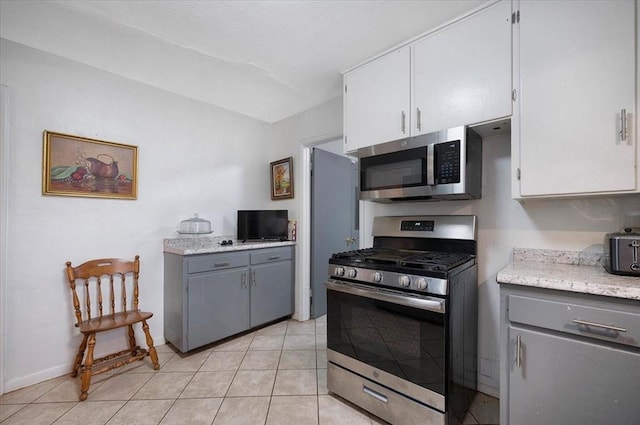 kitchen with stainless steel appliances, white cabinetry, vaulted ceiling, gray cabinetry, and light tile patterned floors