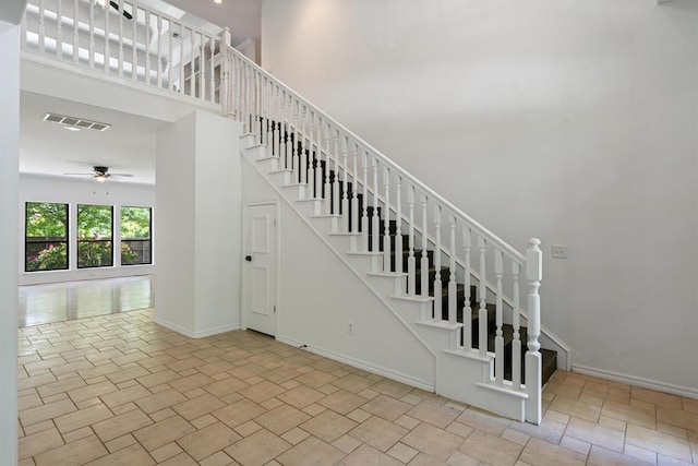 staircase with a ceiling fan, a towering ceiling, and baseboards