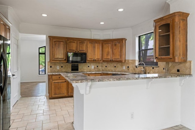 kitchen with black appliances, a sink, healthy amount of natural light, light stone counters, and recessed lighting