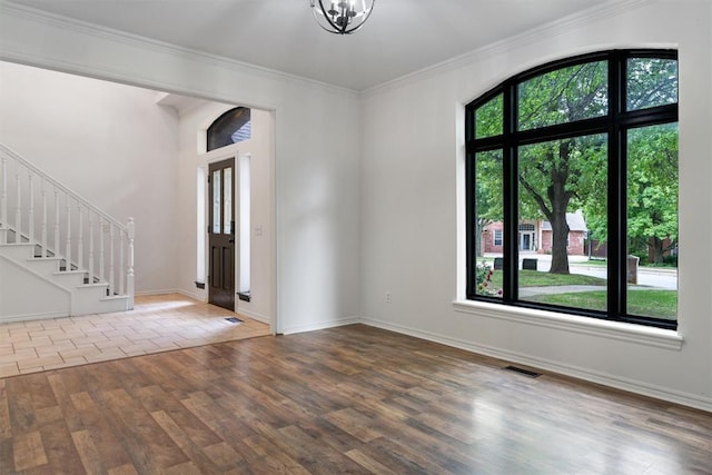 empty room with healthy amount of natural light, stairs, wood finished floors, ornamental molding, and baseboards