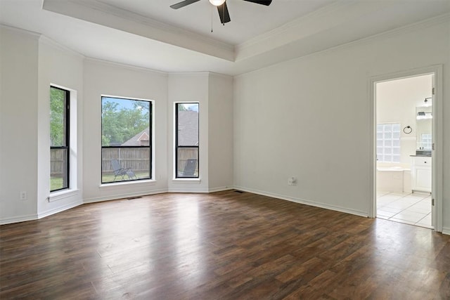 empty room with a tray ceiling, dark wood-type flooring, a ceiling fan, ornamental molding, and baseboards