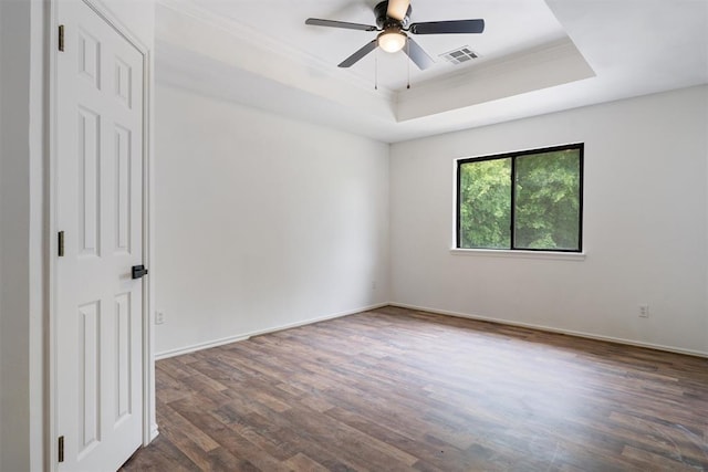 empty room with a raised ceiling, dark wood-style flooring, crown molding, ceiling fan, and baseboards