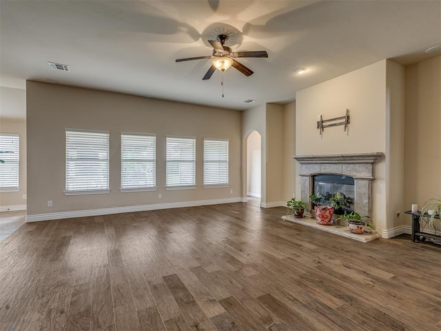 unfurnished living room with arched walkways, ceiling fan, wood finished floors, and a premium fireplace