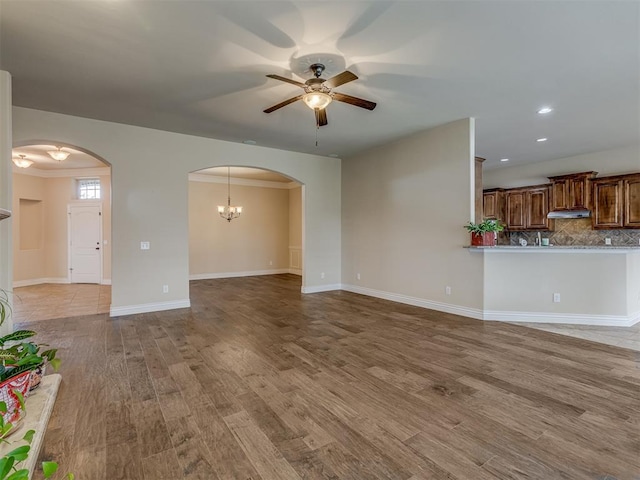 unfurnished living room with ceiling fan, arched walkways, wood finished floors, baseboards, and recessed lighting