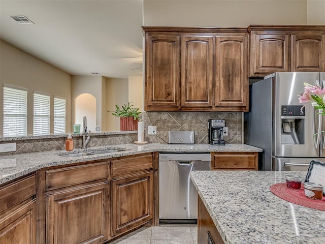 kitchen featuring stainless steel appliances, a sink, light stone countertops, arched walkways, and tasteful backsplash