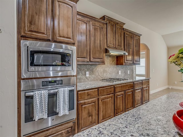 kitchen with stainless steel appliances, tasteful backsplash, light stone counters, under cabinet range hood, and baseboards