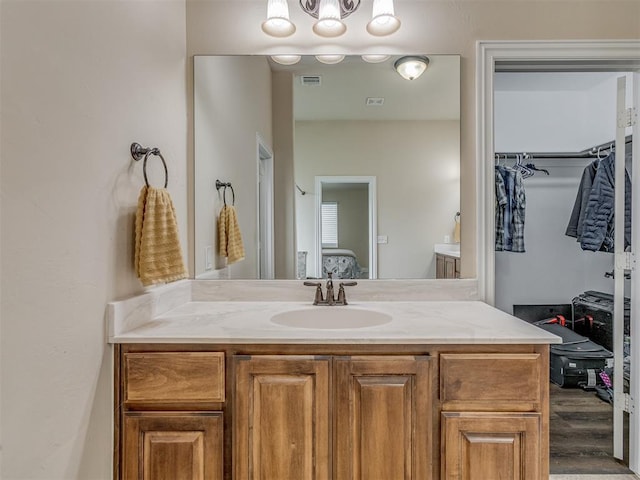 ensuite bathroom featuring vanity, wood finished floors, and a walk in closet