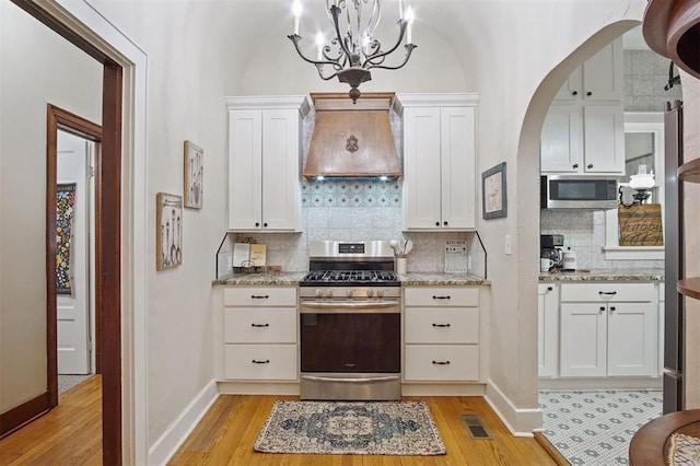 3715 N Mckinley Ave, Oklahoma City, OK 73118 - kitchen with stainless steel appliances, custom exhaust hood, light wood finished floors, and arched walkways