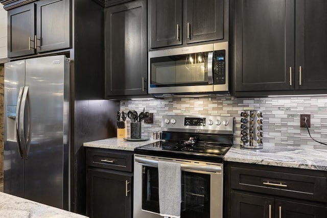 kitchen with stainless steel appliances, tasteful backsplash, light stone countertops, and dark cabinets