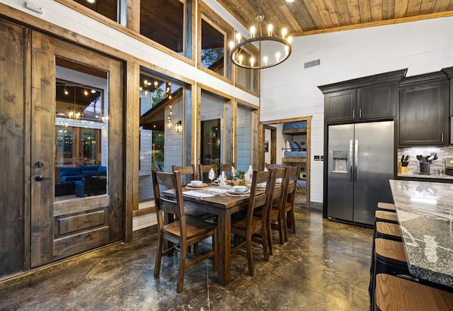 dining room with wood ceiling, a chandelier, wood walls, concrete flooring, and high vaulted ceiling