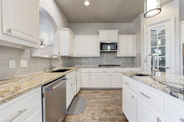 3401 Fox Hill Ter, Edmond, OK 73034 - kitchen featuring stainless steel appliances, arched walkways, wood finished floors, white cabinets, and light stone countertops