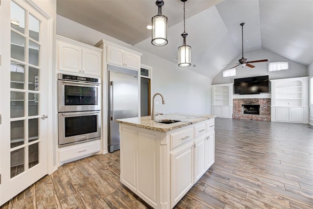 3401 Fox Hill Ter, Edmond, OK 73034 - kitchen featuring stainless steel appliances, ceiling fan, vaulted ceiling, light stone countertops, and a brick fireplace