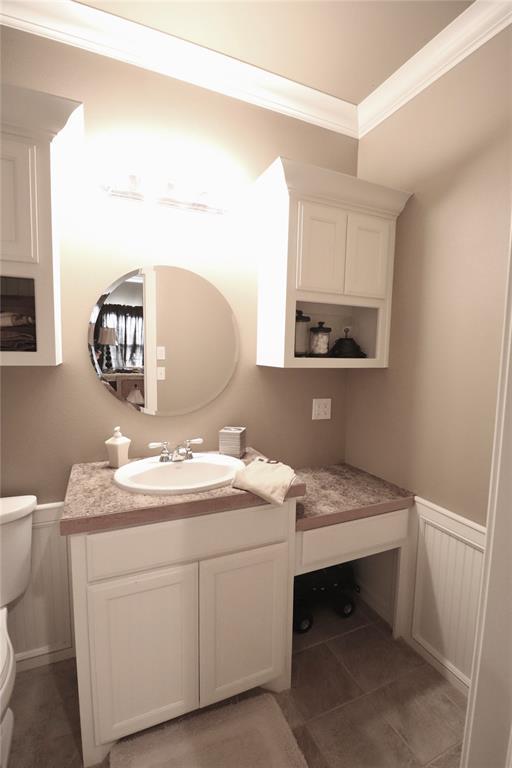 half bath with crown molding, toilet, wainscoting, vanity, and a decorative wall