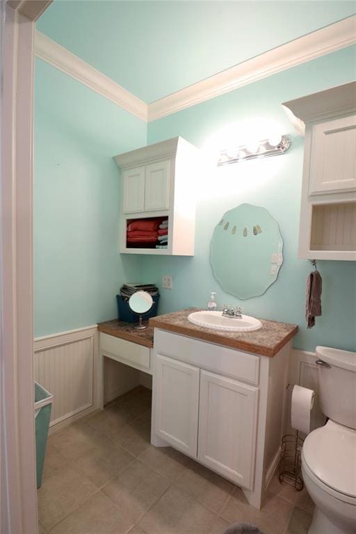 bathroom with a wainscoted wall, ornamental molding, toilet, vanity, and tile patterned floors
