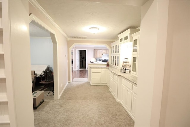 hallway featuring ornamental molding, light colored carpet, arched walkways, and baseboards
