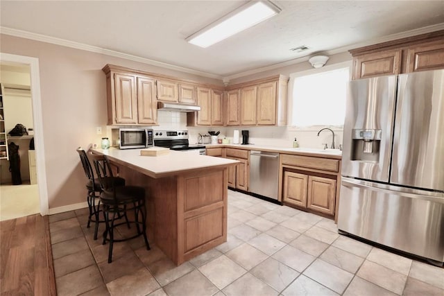 kitchen with stainless steel appliances, under cabinet range hood, a sink, a breakfast bar, and a peninsula