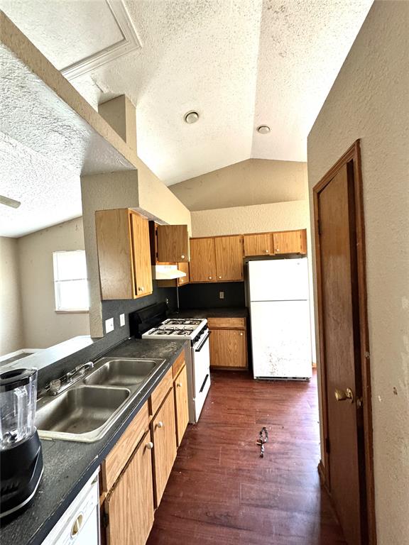 kitchen featuring white appliances, a sink, dark countertops, a textured ceiling, and under cabinet range hood