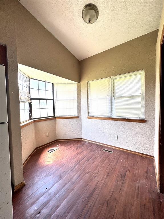 spare room with a textured wall, lofted ceiling, wood finished floors, baseboards, and a textured ceiling