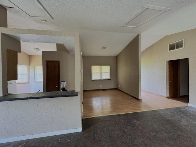 unfurnished living room featuring baseboards, a textured ceiling, wood finished floors, vaulted ceiling, and attic access
