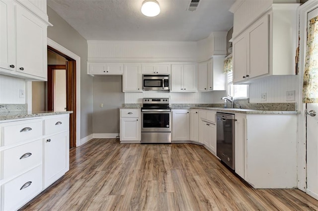 100 S Macomb Ave, El Reno, OK 73036 - kitchen with appliances with stainless steel finishes, light wood-style floors, white cabinetry, and a sink