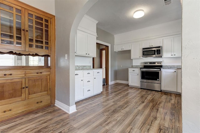 100 S Macomb Ave, El Reno, OK 73036 - kitchen featuring stainless steel appliances, light wood-style flooring, baseboards, white cabinetry, and arched walkways