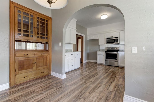100 S Macomb Ave, El Reno, OK 73036 - kitchen featuring appliances with stainless steel finishes, arched walkways, white cabinetry, and wood finished floors