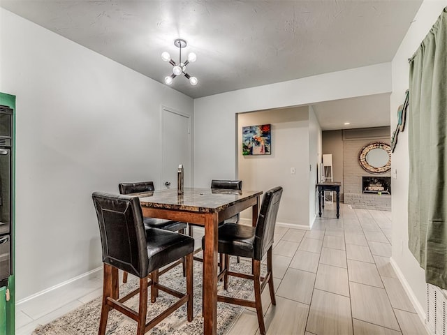 dining space with baseboards, a chandelier, and a brick fireplace