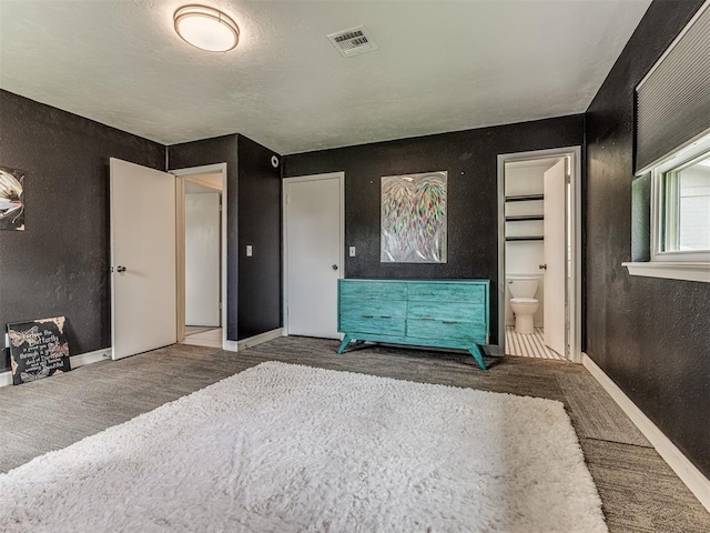 unfurnished bedroom with baseboards, a textured wall, carpet floors, ensuite bath, and wood finished floors