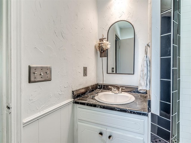 bathroom with vanity, a textured wall, and a wainscoted wall