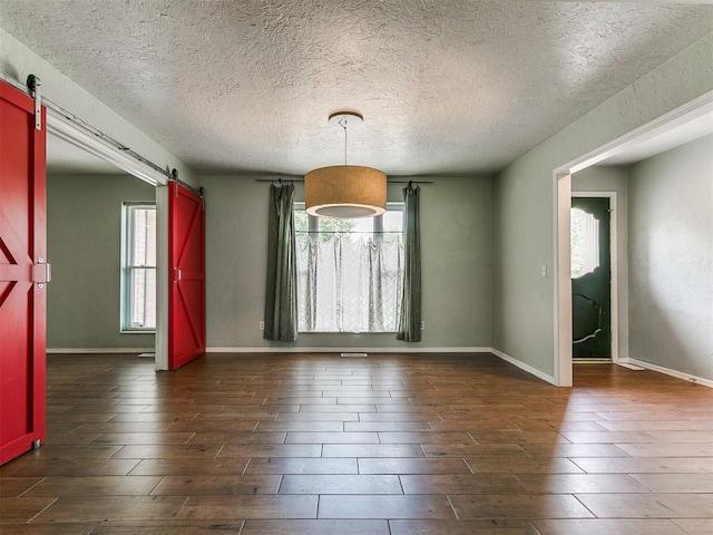 2916 Prairie Rose Ct, Oklahoma City, OK 73120 - unfurnished dining area featuring a barn door, dark wood-type flooring, a textured ceiling, and baseboards